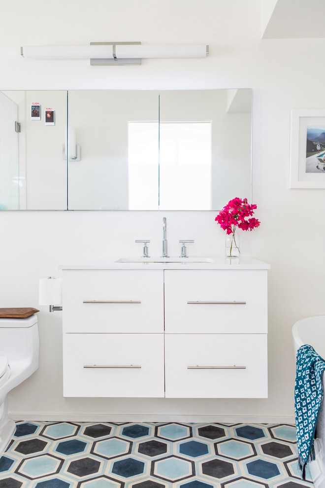 Photo of a mid-sized transitional master bathroom in Los Angeles with flat-panel cabinets, white cabinets, a freestanding tub, an alcove shower, a one-piece toilet, blue tile, cement tile, white walls, concrete floors, an undermount sink and engineered quartz benchtops.