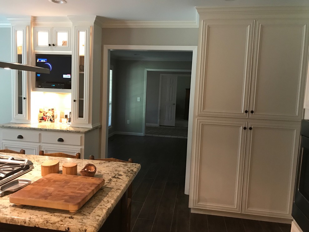 Eat-in kitchen - large transitional l-shaped brown floor eat-in kitchen idea in Birmingham with a farmhouse sink, recessed-panel cabinets, white cabinets, beige backsplash, stainless steel appliances and an island