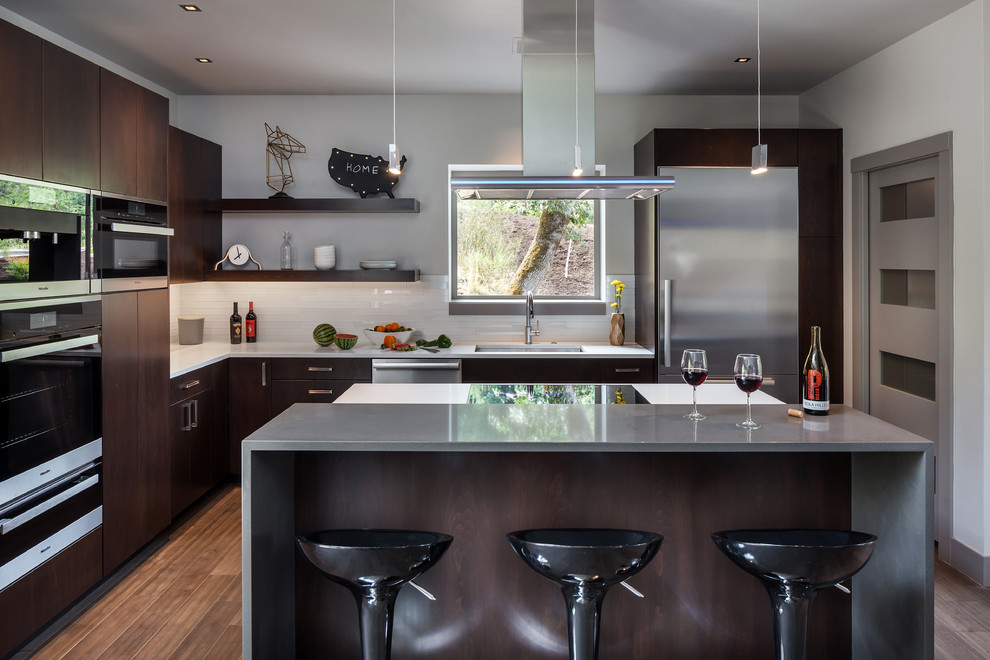 Large contemporary l-shaped open plan kitchen in Portland with an undermount sink, flat-panel cabinets, dark wood cabinets, white splashback, stainless steel appliances, dark hardwood floors, with island, quartz benchtops and glass tile splashback.