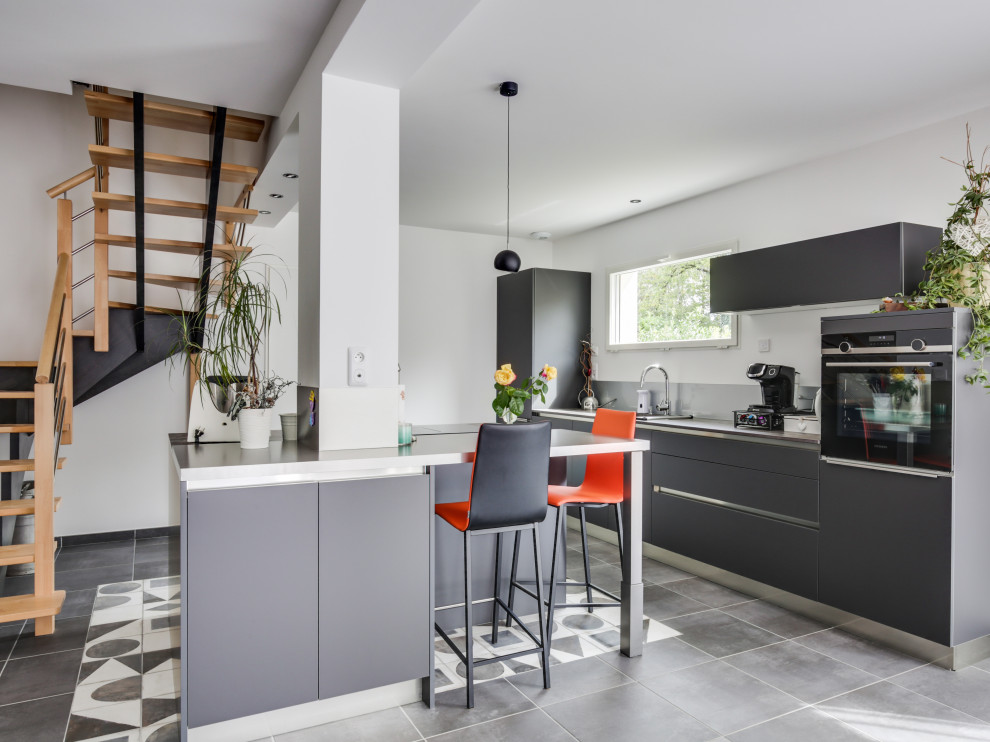 Design ideas for a contemporary l-shaped kitchen in Lyon with flat-panel cabinets, grey cabinets, black appliances, with island, grey floor and grey benchtop.