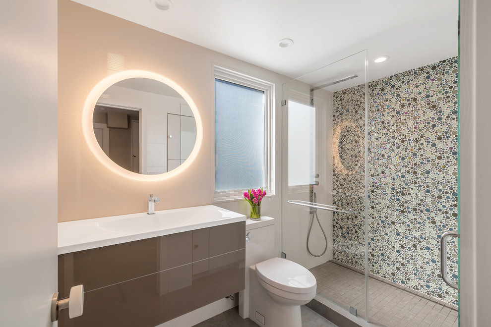 Photo of a small contemporary 3/4 bathroom in San Francisco with flat-panel cabinets, brown cabinets, an alcove shower, a one-piece toilet, multi-coloured tile, glass tile, white walls, porcelain floors, an integrated sink, glass benchtops, grey floor, a hinged shower door and white benchtops.