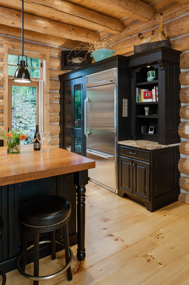 Inspiration for a rustic l-shaped eat-in kitchen remodel with an undermount sink, raised-panel cabinets, black cabinets, wood countertops, multicolored backsplash, stone slab backsplash and stainless steel appliances