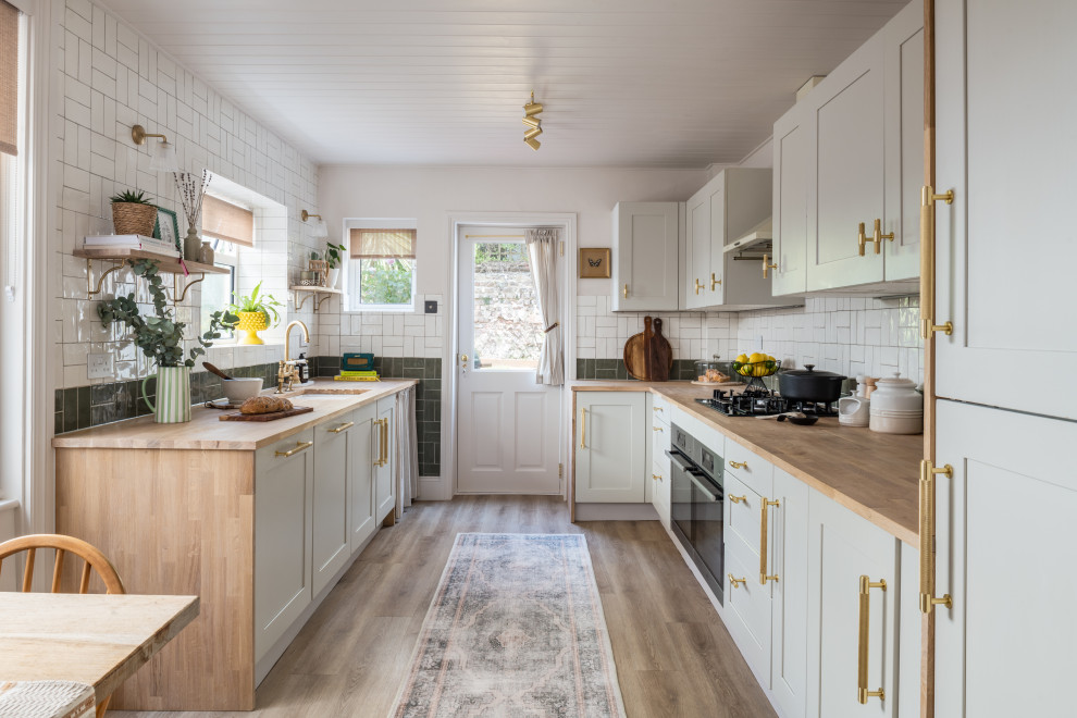 Medium sized farmhouse grey and white galley kitchen/diner in Sussex with shaker cabinets, grey cabinets, wood worktops, green splashback, vinyl flooring, no island, a timber clad ceiling and feature lighting.