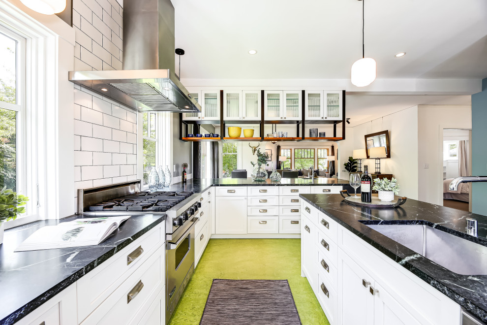 This is an example of a mid-sized transitional l-shaped eat-in kitchen in Seattle with an undermount sink, recessed-panel cabinets, white cabinets, marble benchtops, white splashback, porcelain splashback, stainless steel appliances, linoleum floors, a peninsula, green floor and black benchtop.