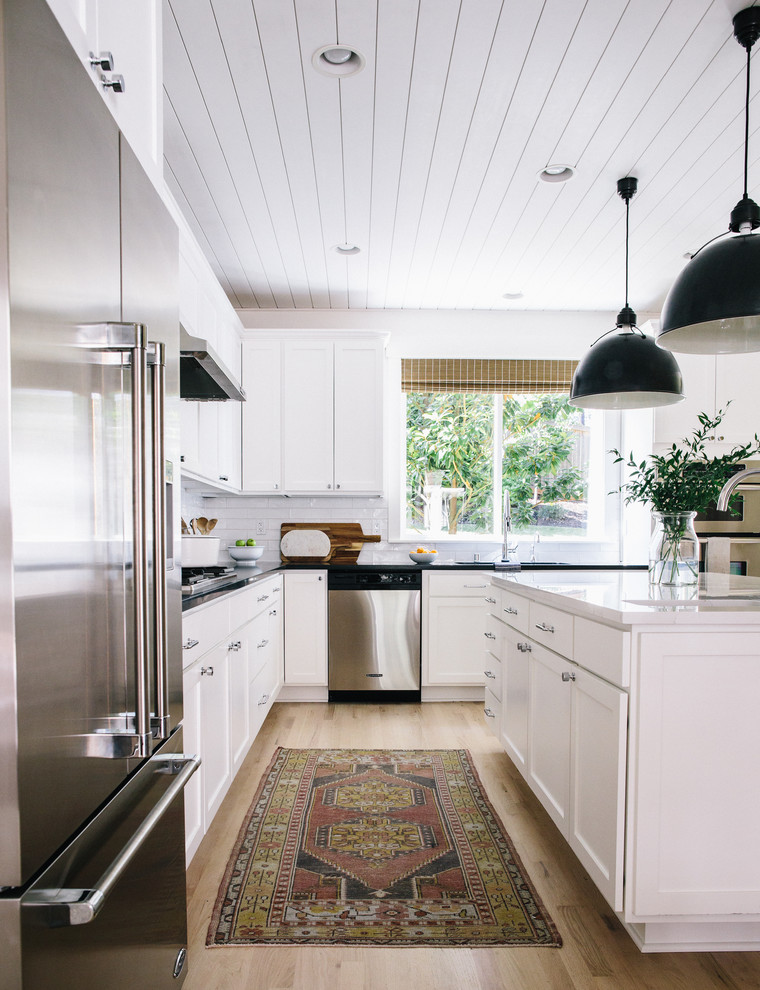 Design ideas for a mid-sized country l-shaped kitchen in Seattle with an undermount sink, shaker cabinets, white cabinets, quartz benchtops, white splashback, ceramic splashback, stainless steel appliances, light hardwood floors, with island, beige floor and white benchtop.