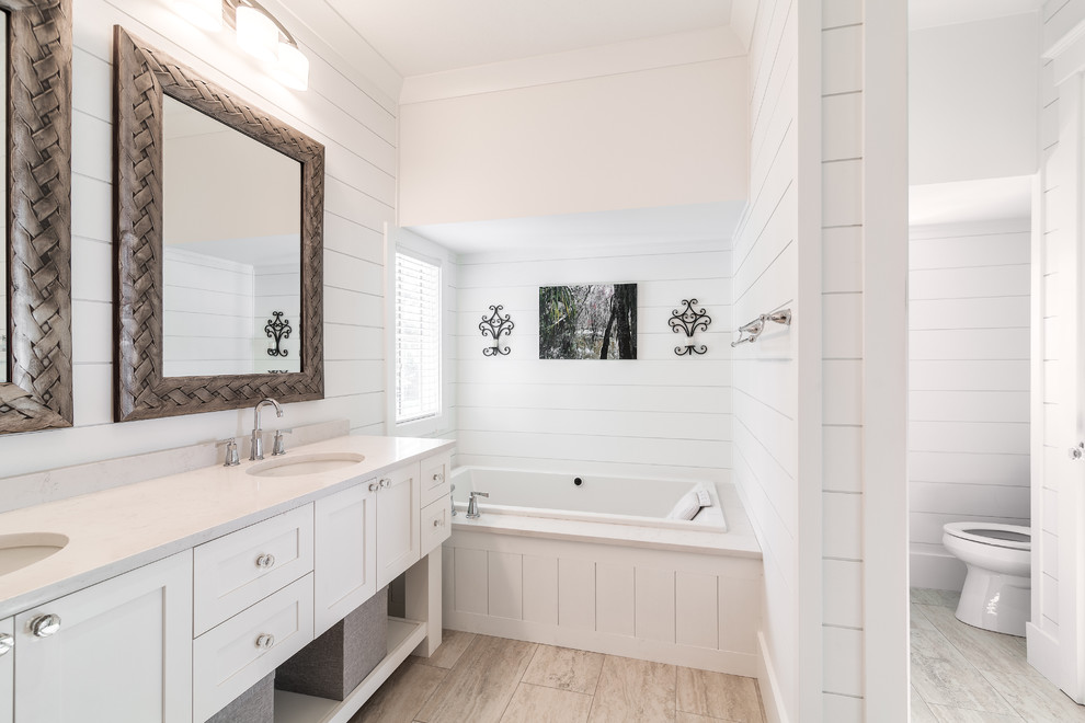 Inspiration for a mid-sized beach style master bathroom in Atlanta with an undermount sink, shaker cabinets, white cabinets, solid surface benchtops, a drop-in tub, a one-piece toilet, white tile, white walls and ceramic floors.