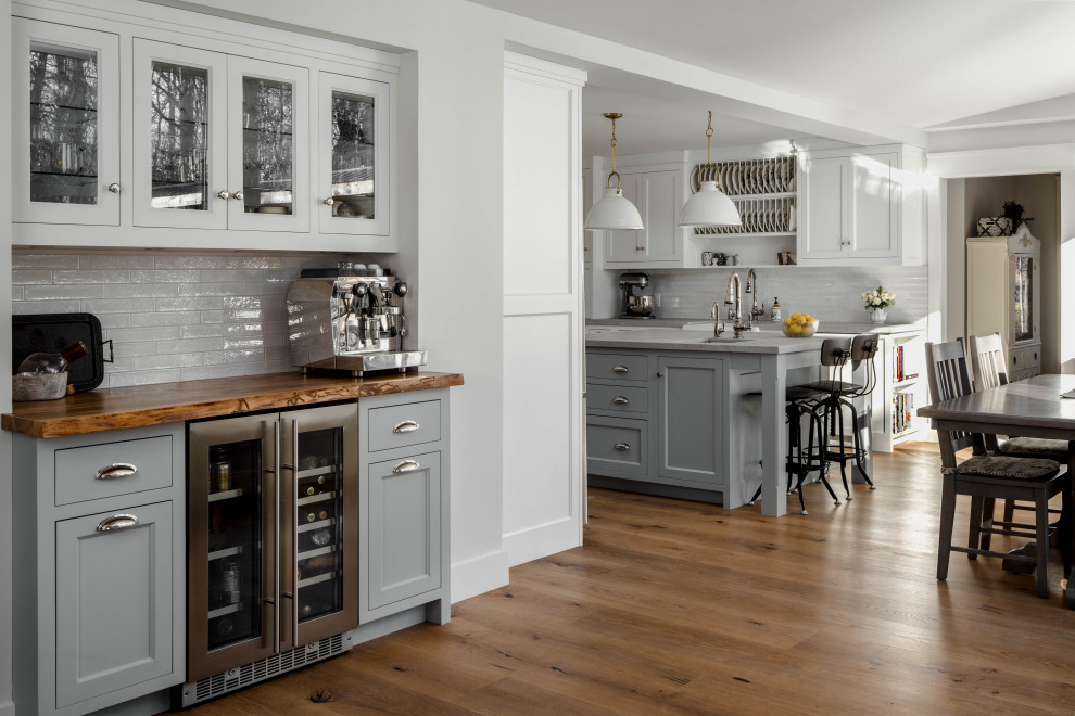 Inspiration for a large transitional l-shaped eat-in kitchen in Toronto with a farmhouse sink, recessed-panel cabinets, white cabinets, marble benchtops, white splashback, subway tile splashback, stainless steel appliances, light hardwood floors, with island, brown floor and grey benchtop.