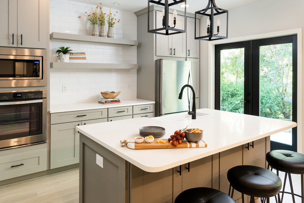 Design ideas for a large transitional single-wall open plan kitchen with a farmhouse sink, shaker cabinets, grey cabinets, quartz benchtops, white splashback, ceramic splashback, stainless steel appliances, light hardwood floors, with island, yellow floor and white benchtop.