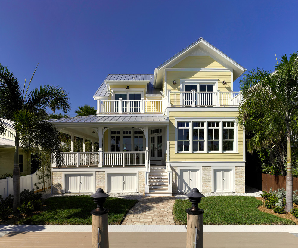 This is an example of a large traditional two-storey yellow house exterior in Tampa with concrete fiberboard siding, a gable roof and a metal roof.