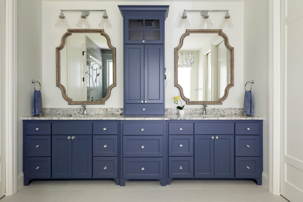 This is an example of a large beach style master bathroom in Minneapolis with shaker cabinets, blue cabinets, white walls, porcelain floors, granite benchtops, grey floor, multi-coloured benchtops, a double vanity and a built-in vanity.