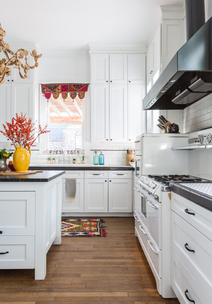 This is an example of a mid-sized transitional u-shaped eat-in kitchen in Houston with shaker cabinets, white cabinets, white splashback, subway tile splashback, white appliances, medium hardwood floors, with island, brown floor and tile benchtops.