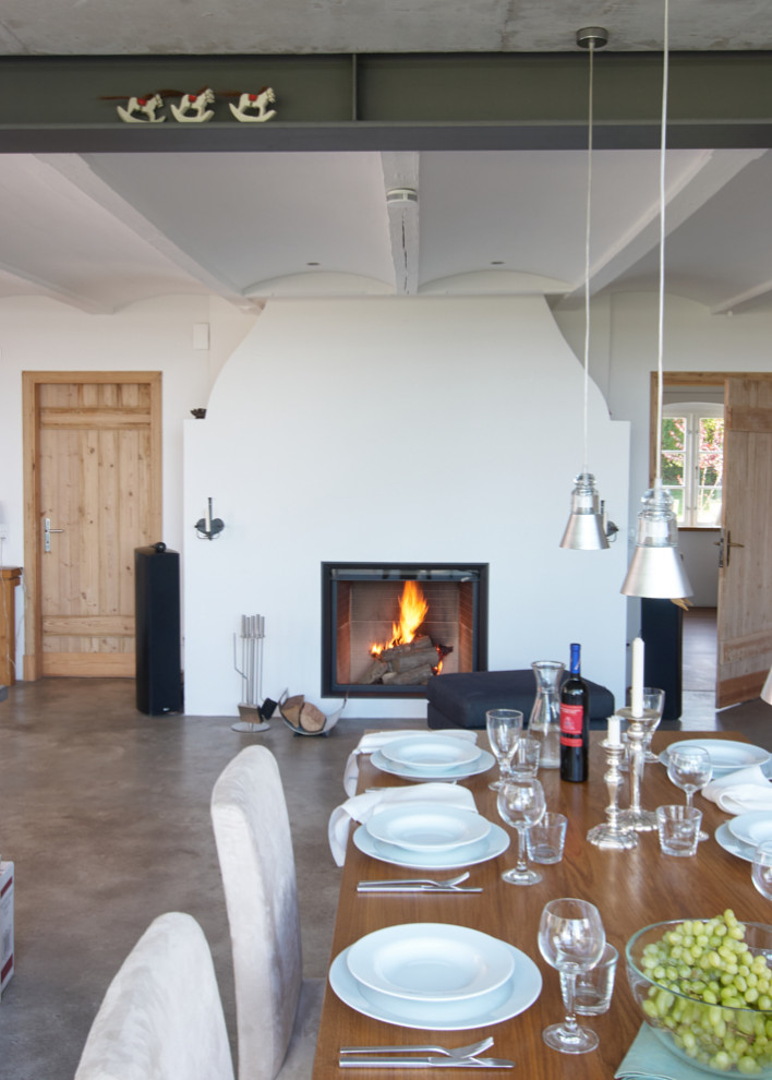 Design ideas for a large country open plan dining in Hamburg with white walls, concrete floors, a standard fireplace, a plaster fireplace surround, grey floor and vaulted.