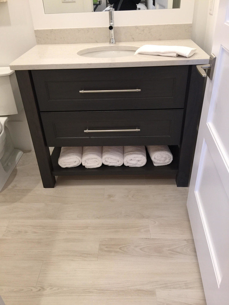 Mid-sized transitional 3/4 light wood floor and beige floor bathroom photo in Miami with shaker cabinets, a one-piece toilet, white walls, an undermount sink, soapstone countertops and black cabinets