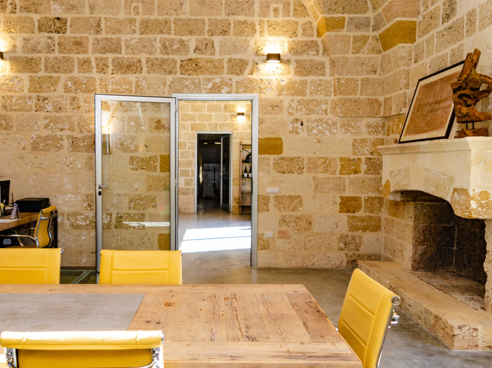 Стильный дизайн: рабочее место в средиземноморском стиле с бетонным полом, стандартным камином, фасадом камина из камня, отдельно стоящим рабочим столом, серым полом и сводчатым потолком - последний тренд