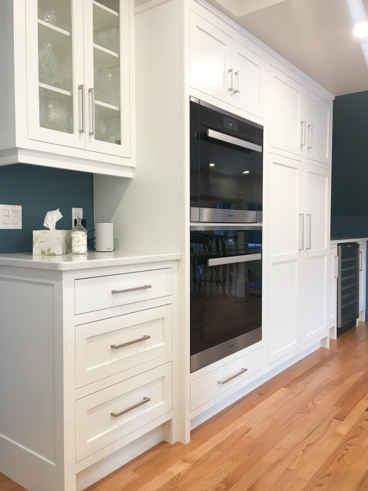 Large transitional u-shaped light wood floor and beige floor eat-in kitchen photo with a double-bowl sink, shaker cabinets, white cabinets, quartzite countertops, white backsplash, subway tile backsplash, stainless steel appliances, an island and white countertops