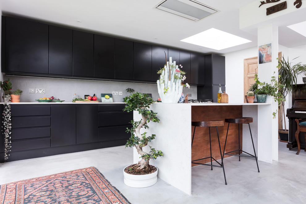 Inspiration for a large eclectic eat-in kitchen in Edinburgh with an integrated sink, flat-panel cabinets, black cabinets, quartzite benchtops, grey splashback, panelled appliances, concrete floors, with island, grey floor and white benchtop.