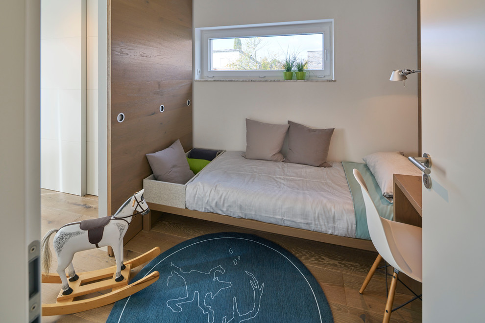 Photo of a small contemporary gender-neutral kids' playroom for kids 4-10 years old in Berlin with white walls, medium hardwood floors and brown floor.