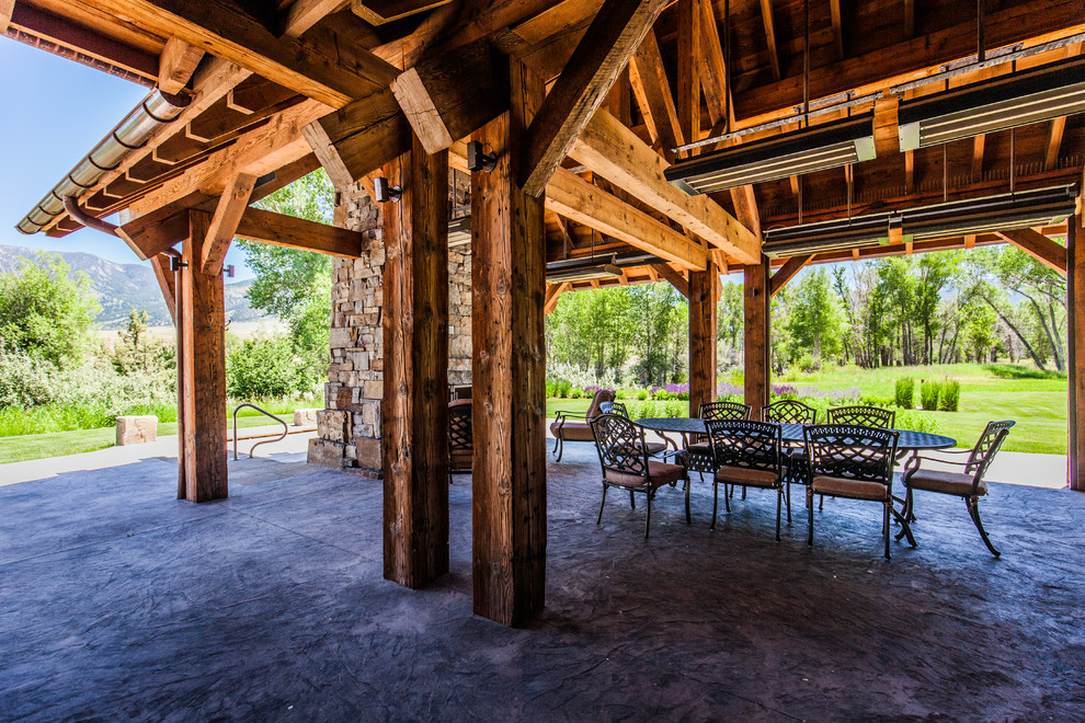 Large mountain style backyard concrete patio photo with a fire pit and a roof extension