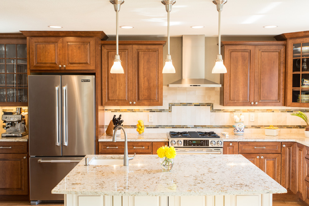 Inspiration for a large transitional l-shaped medium tone wood floor and brown floor eat-in kitchen remodel in Denver with a farmhouse sink, raised-panel cabinets, medium tone wood cabinets, granite countertops, beige backsplash, stone tile backsplash, stainless steel appliances and an island