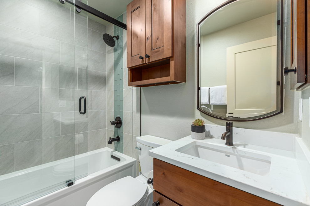 Mid-sized transitional kids bathroom in Denver with beaded inset cabinets, medium wood cabinets, an alcove tub, a shower/bathtub combo, a two-piece toilet, white tile, ceramic tile, white walls, an undermount sink, engineered quartz benchtops, a sliding shower screen, white benchtops, a single vanity and a built-in vanity.