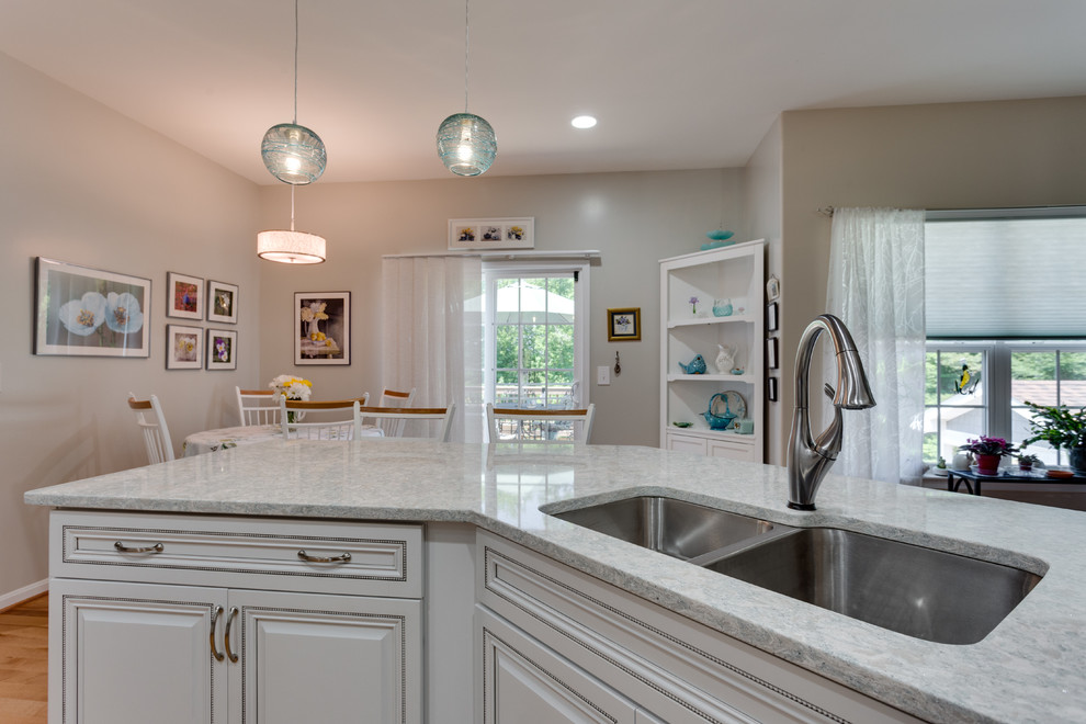 This is an example of a mid-sized transitional u-shaped kitchen in DC Metro with an undermount sink, raised-panel cabinets, white cabinets, quartz benchtops, stainless steel appliances, medium hardwood floors and no island.