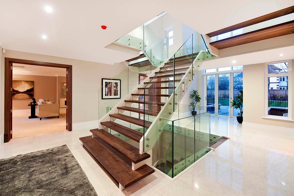 Design ideas for a contemporary wood u-shaped staircase in London with open risers and glass railing.