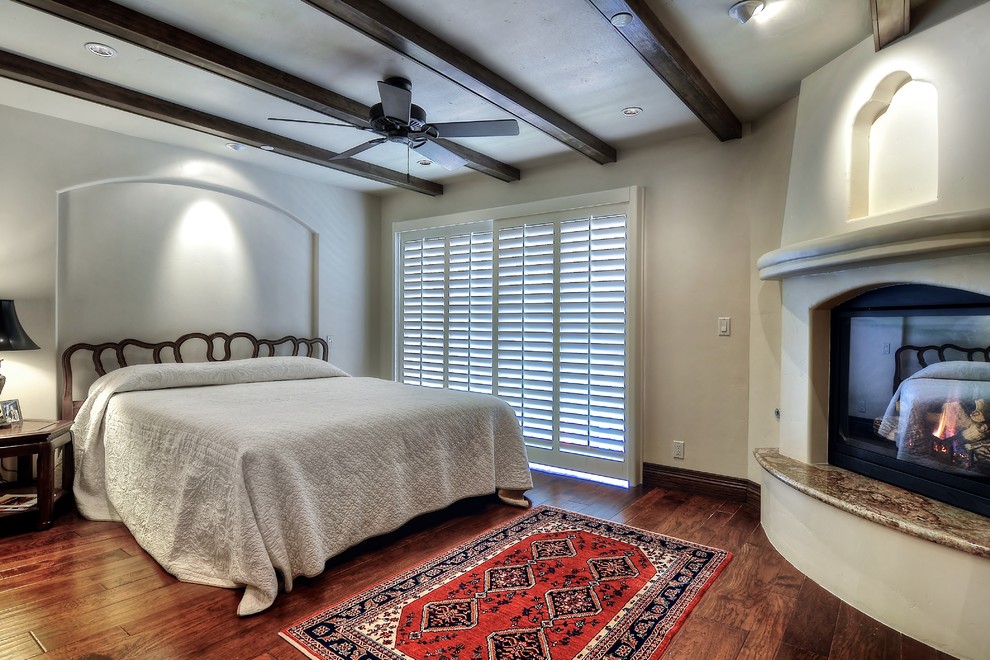 Inspiration for a large mediterranean guest bedroom in Orange County with a corner fireplace, white walls, dark hardwood floors, a plaster fireplace surround and brown floor.