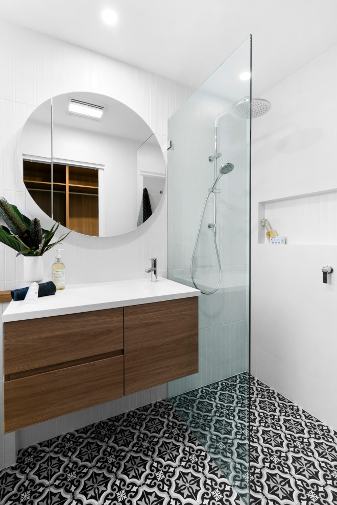 This is an example of a mid-sized beach style master bathroom in Sydney with furniture-like cabinets, medium wood cabinets, a freestanding tub, a shower/bathtub combo, a two-piece toilet, white tile, porcelain tile, white walls, porcelain floors, an integrated sink, solid surface benchtops, blue floor, an open shower, white benchtops, a niche, a single vanity, a floating vanity and planked wall panelling.