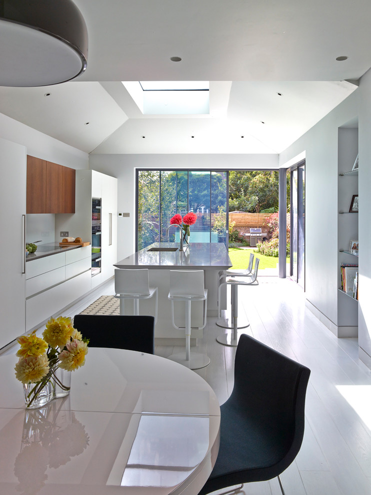 Mid-sized contemporary single-wall eat-in kitchen in London with flat-panel cabinets, solid surface benchtops, glass sheet splashback, painted wood floors, with island, white floor and beige benchtop.