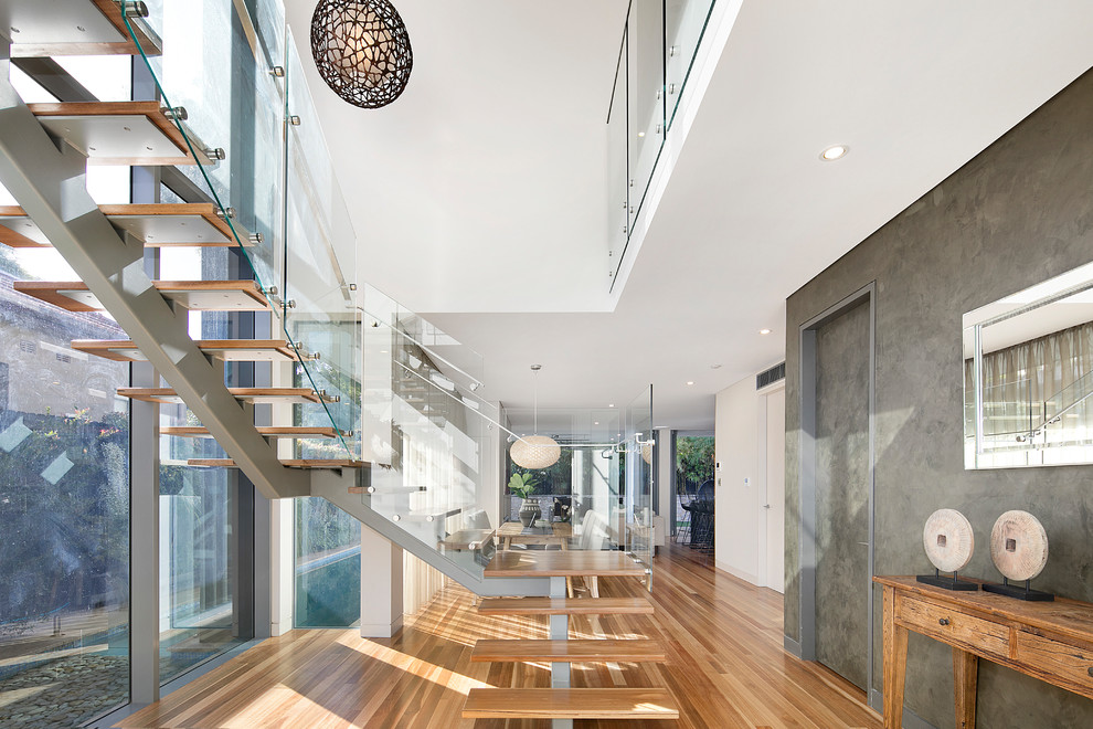 Photo of a large contemporary wood u-shaped staircase in Sydney with glass railing and open risers.