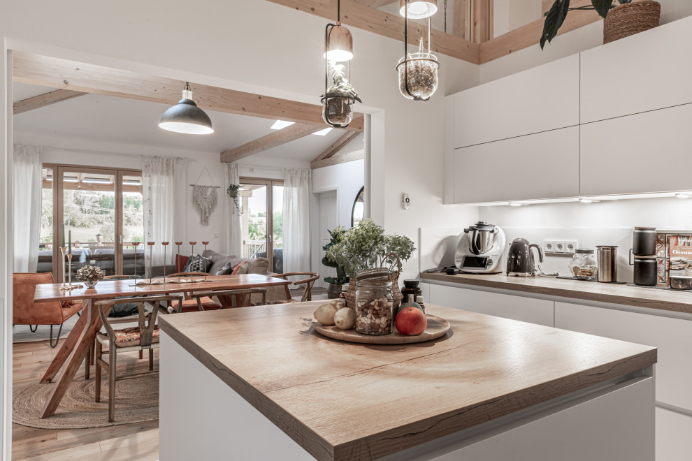 Inspiration for a mid-sized country u-shaped open plan kitchen in Bonn with flat-panel cabinets, white cabinets, wood benchtops, white splashback, light hardwood floors and wood.