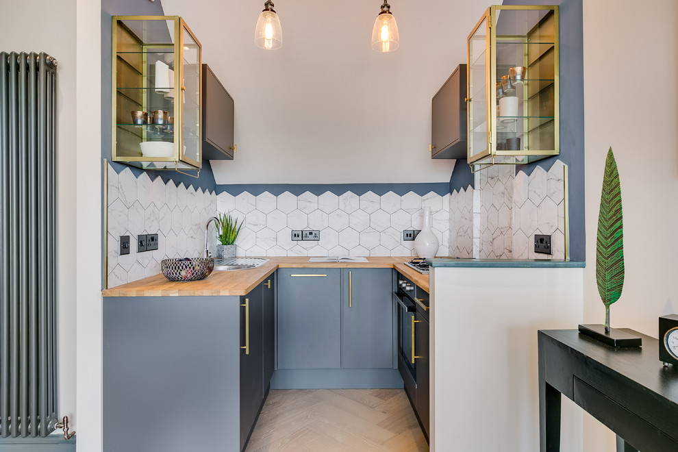 Photo of a contemporary u-shaped kitchen in London with a drop-in sink, flat-panel cabinets, grey cabinets, wood benchtops, white splashback, black appliances, beige floor and brown benchtop.