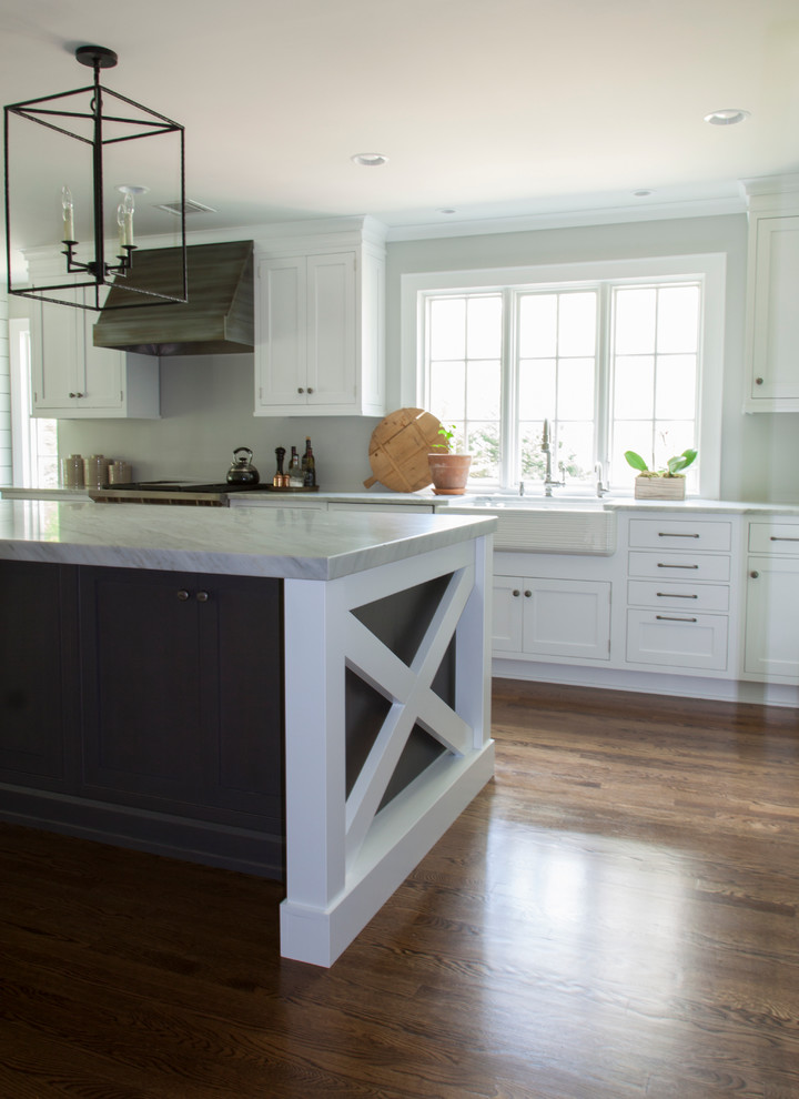 Inspiration for a large transitional l-shaped dark wood floor enclosed kitchen remodel in Newark with a farmhouse sink, shaker cabinets, white cabinets, marble countertops, white backsplash, stainless steel appliances and an island