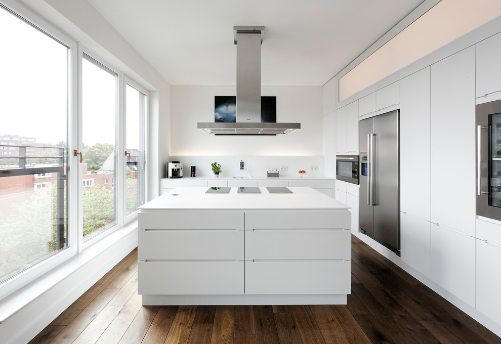 Inspiration for a large contemporary l-shaped open plan kitchen in Hamburg with an integrated sink, flat-panel cabinets, white cabinets, solid surface benchtops, white splashback, stainless steel appliances, dark hardwood floors, with island, glass sheet splashback and brown floor.