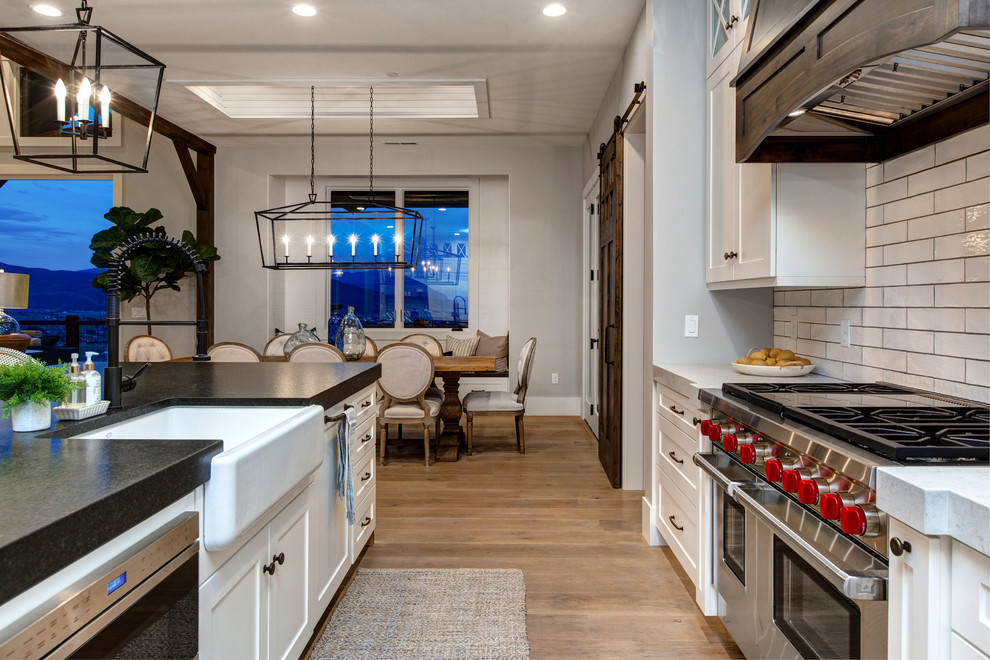 Inspiration for a large country single-wall open plan kitchen in Salt Lake City with a farmhouse sink, shaker cabinets, white cabinets, soapstone benchtops, white splashback, subway tile splashback, stainless steel appliances, medium hardwood floors and with island.