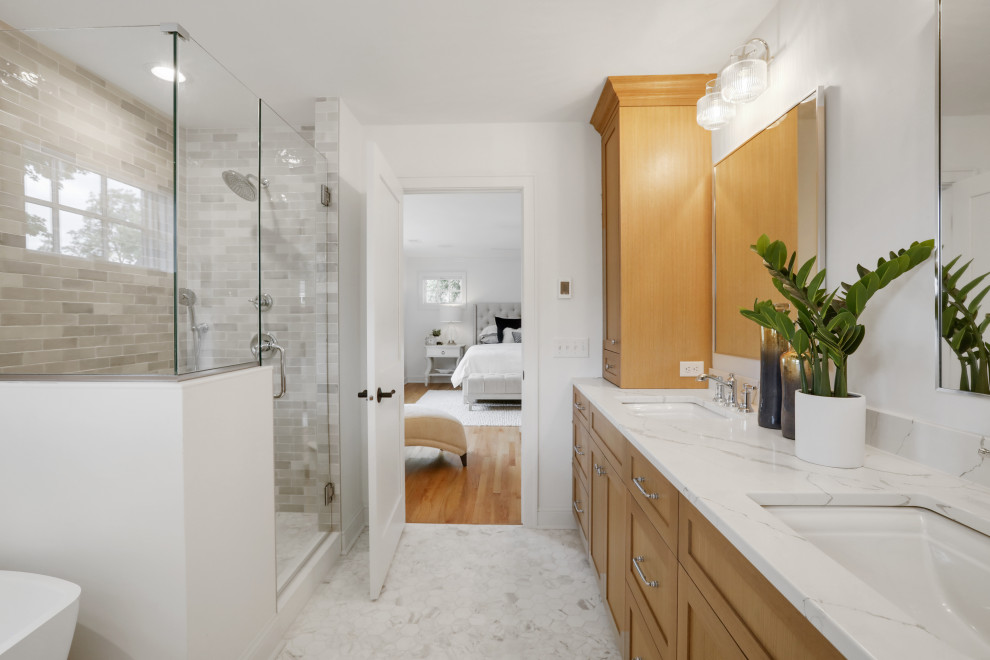 This is an example of a medium sized classic ensuite bathroom in Minneapolis with recessed-panel cabinets, light wood cabinets, a freestanding bath, a corner shower, a two-piece toilet, multi-coloured tiles, ceramic tiles, white walls, marble flooring, a submerged sink, engineered stone worktops, white floors, a hinged door, white worktops, double sinks and a built in vanity unit.