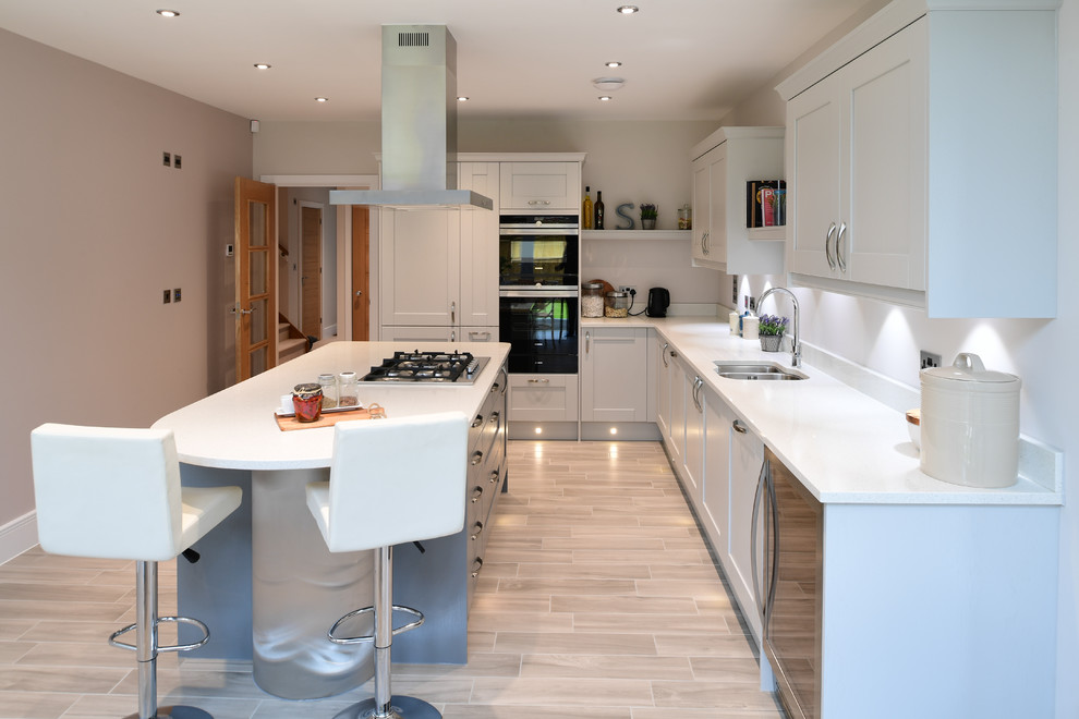 Mid-sized transitional l-shaped separate kitchen in London with porcelain floors, beige floor, a double-bowl sink, white cabinets, with island, white benchtop, shaker cabinets, white splashback and black appliances.