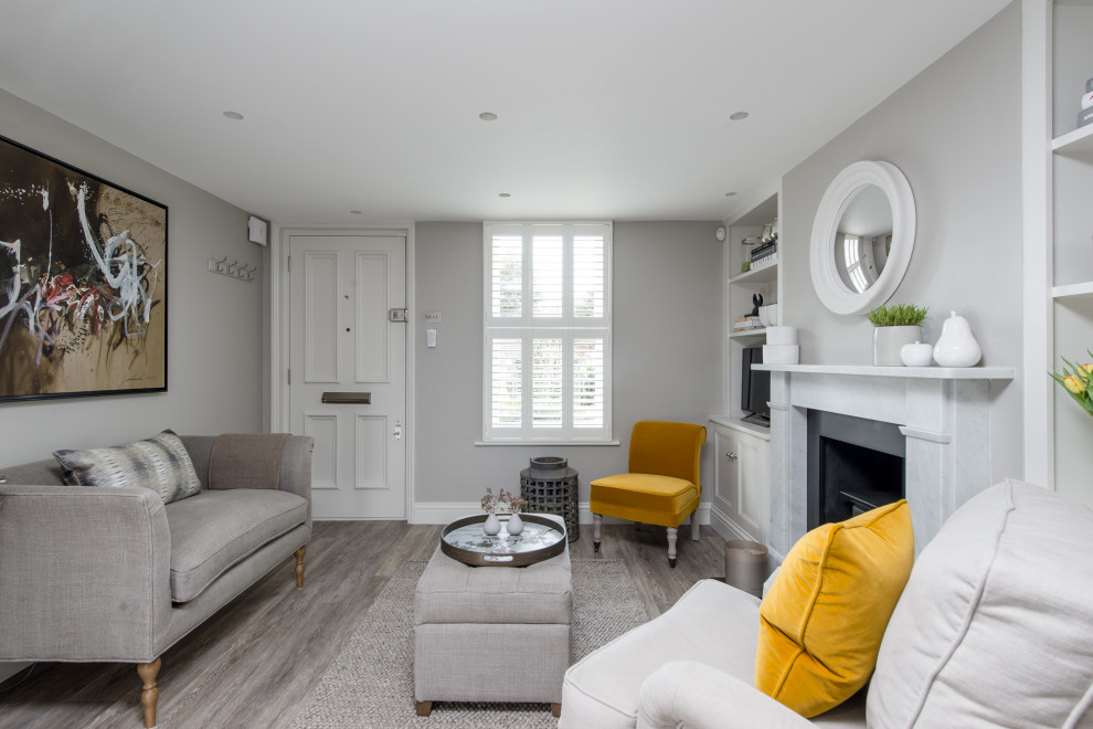 This is an example of a small transitional open concept living room in London with grey walls, medium hardwood floors, a standard fireplace, a stone fireplace surround and grey floor.