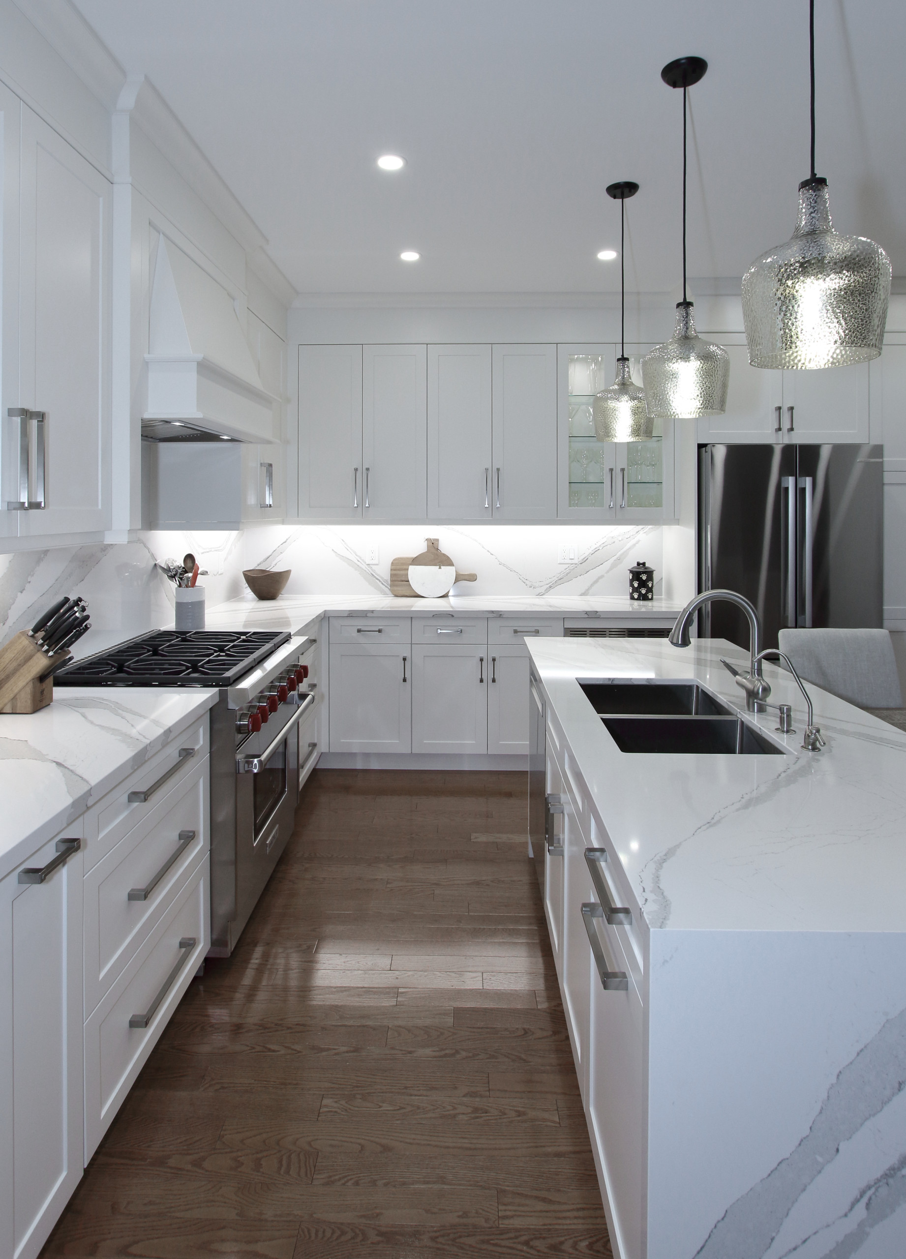 Example of a mid-sized transitional l-shaped medium tone wood floor open concept kitchen design in Toronto with an undermount sink, shaker cabinets, white cabinets, quartz countertops, white backsplas