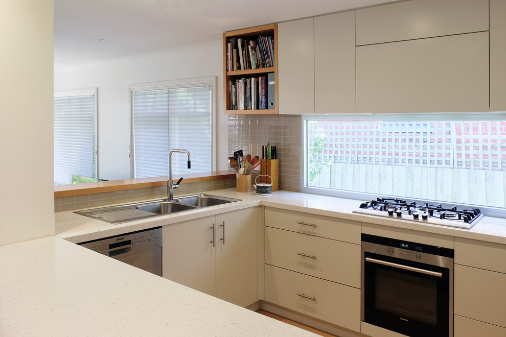 Mid-sized contemporary u-shaped eat-in kitchen in Melbourne with a drop-in sink, flat-panel cabinets, quartz benchtops, stainless steel appliances, medium hardwood floors, a peninsula, white cabinets and window splashback.