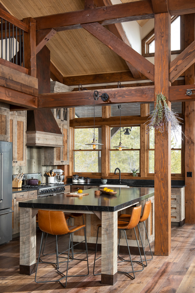 Design ideas for a country l-shaped open plan kitchen in Denver with shaker cabinets, medium wood cabinets, stainless steel appliances, medium hardwood floors, with island, brown floor and black benchtop.