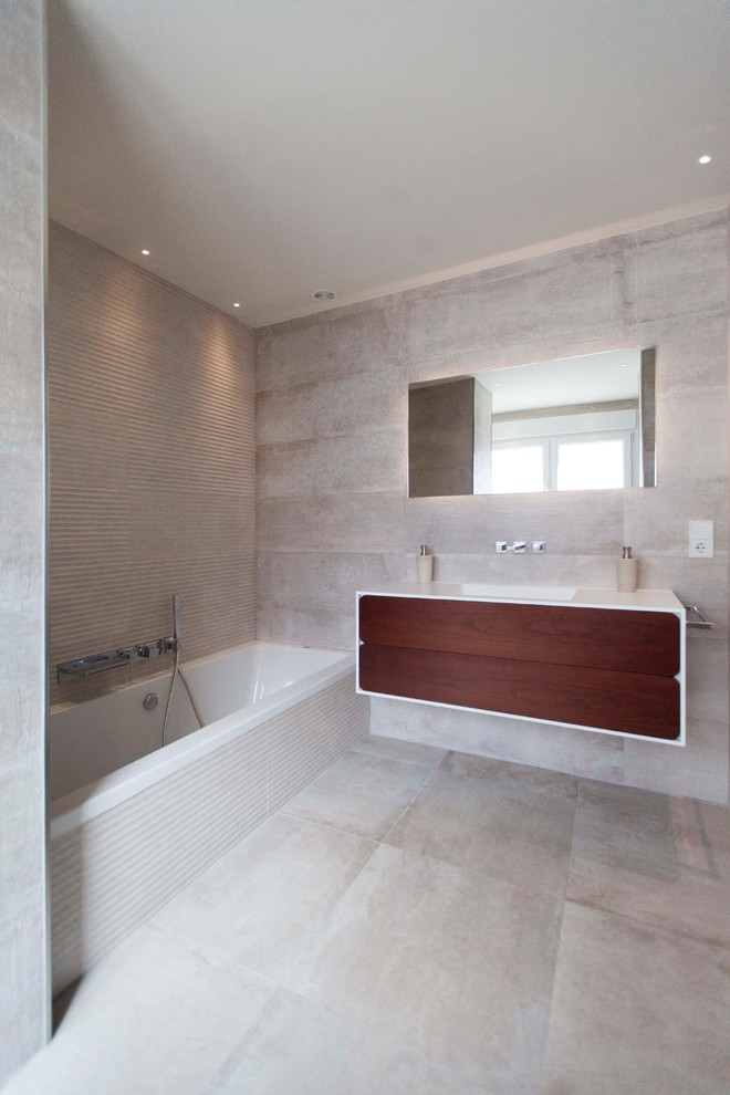 Foto de cuarto de baño principal minimalista grande con armarios con paneles lisos, puertas de armario de madera en tonos medios, bañera empotrada, ducha a ras de suelo, sanitario de dos piezas, baldosas y/o azulejos beige, baldosas y/o azulejos de cerámica, paredes beige, suelo de baldosas de cerámica, lavabo integrado, encimera de acrílico, suelo beige y ducha con puerta con bisagras