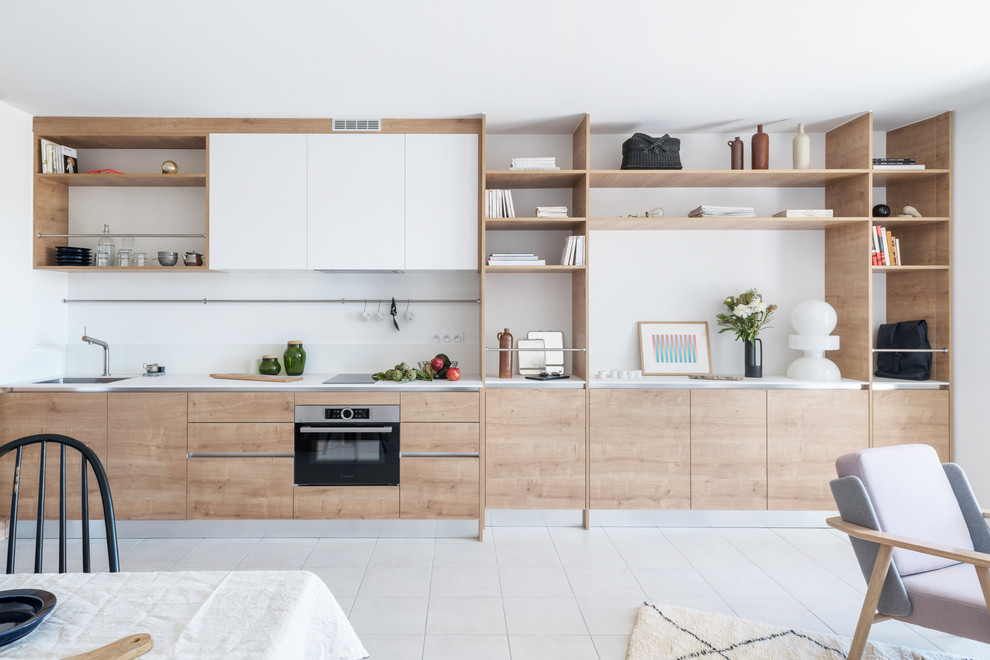 Réalisation d'une cuisine ouverte linéaire nordique en bois brun de taille moyenne avec un placard à porte affleurante, un évier 1 bac, une crédence blanche, un électroménager noir, un sol en carrelage de céramique, aucun îlot, un sol beige et un plan de travail blanc.