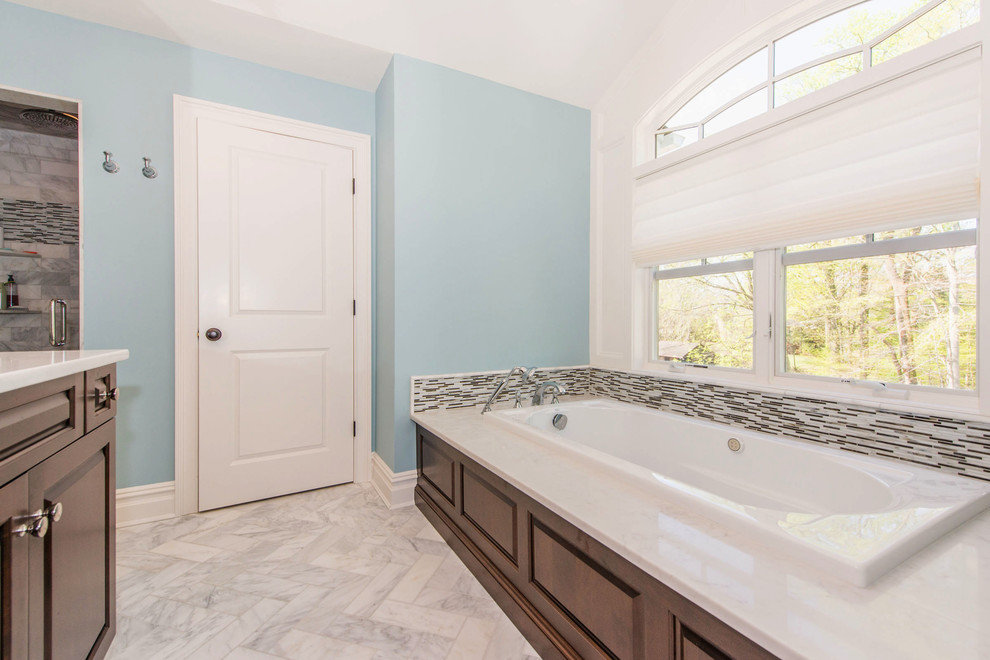Mid-sized traditional master bathroom in New York with a drop-in tub, an alcove shower, a one-piece toilet, beige tile, a hinged shower door, raised-panel cabinets, dark wood cabinets, blue walls, marble floors, an undermount sink, marble benchtops, white floor and white benchtops.