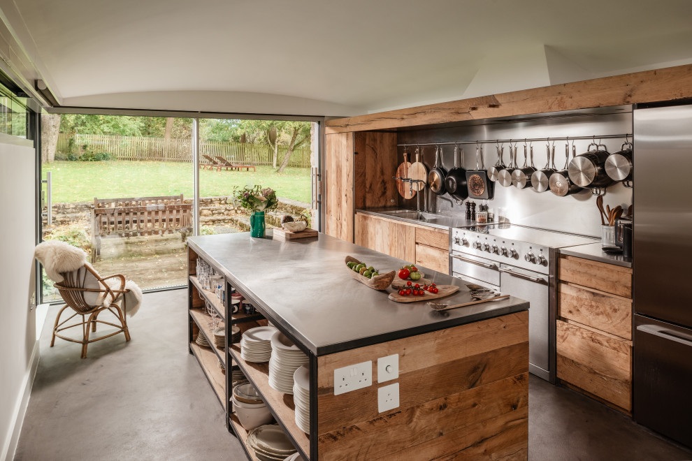 Large country l-shaped open plan kitchen in Oxfordshire with stainless steel worktops, concrete flooring and an island.