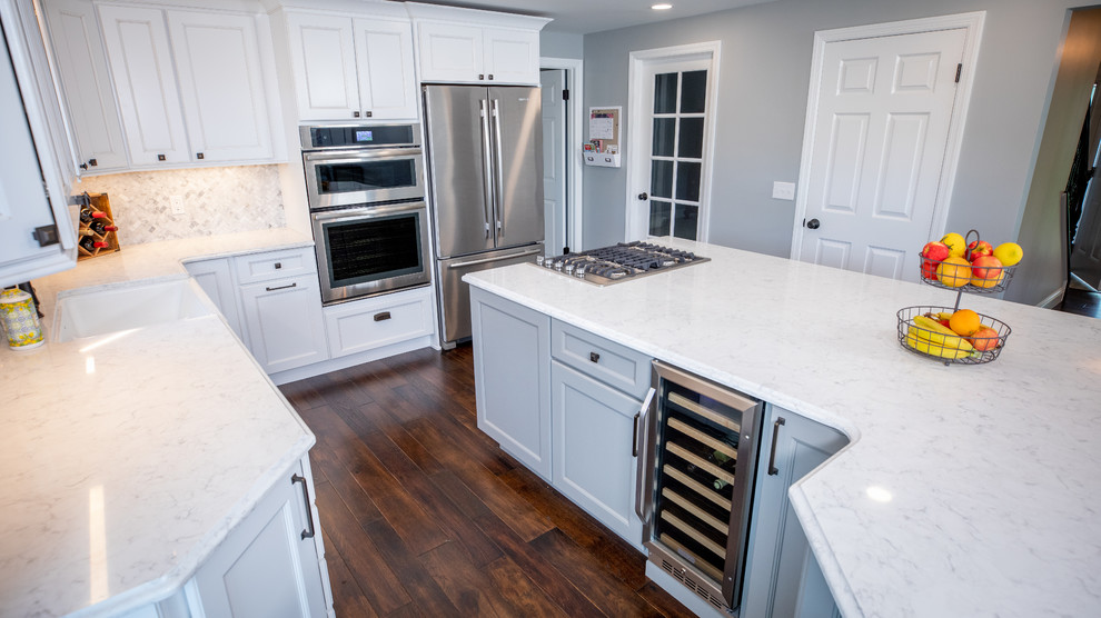 Inspiration for a large transitional u-shaped dark wood floor and brown floor eat-in kitchen remodel with a farmhouse sink, recessed-panel cabinets, white cabinets, quartz countertops, white backsplash, marble backsplash, stainless steel appliances, an island and white countertops