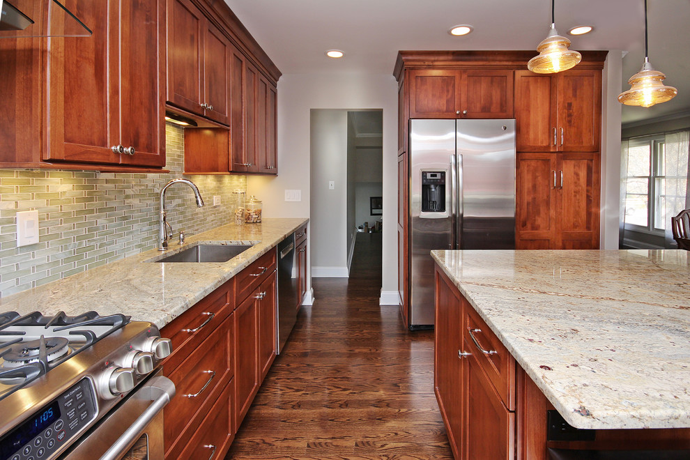 This is an example of a mid-sized transitional l-shaped eat-in kitchen in Chicago with a single-bowl sink, shaker cabinets, medium wood cabinets, granite benchtops, green splashback, glass tile splashback, stainless steel appliances, dark hardwood floors and with island.