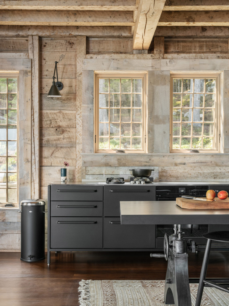 Photo of a beach style galley kitchen in Other with an integrated sink, flat-panel cabinets, black cabinets, stainless steel benchtops, black appliances, dark hardwood floors, brown floor and exposed beam.