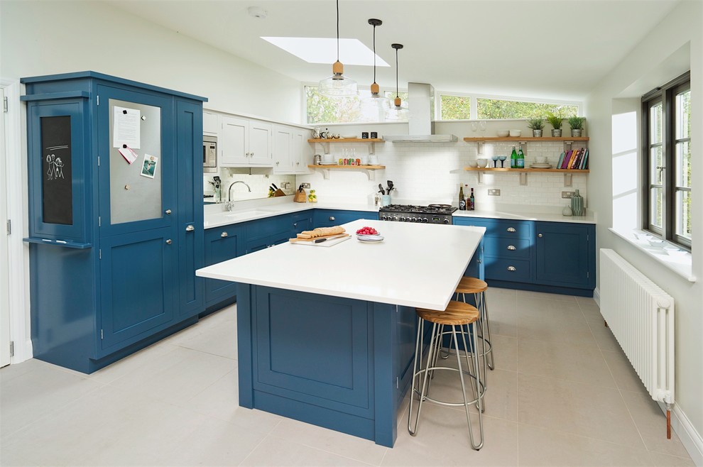 This is an example of a mid-sized transitional u-shaped eat-in kitchen in Hertfordshire with blue cabinets, quartzite benchtops, stainless steel appliances, with island, recessed-panel cabinets, white splashback, subway tile splashback and grey floor.