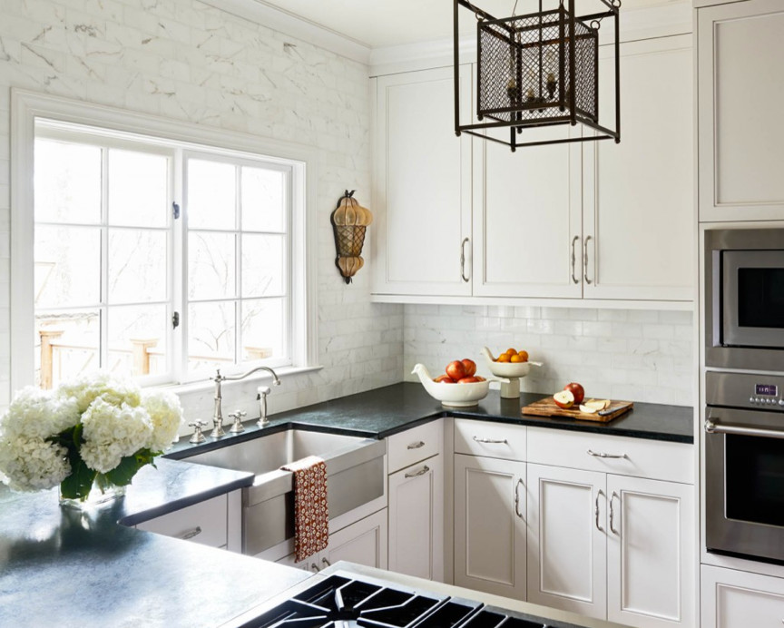 Example of a large transitional u-shaped light wood floor enclosed kitchen design in Charlotte with a farmhouse sink, recessed-panel cabinets, white cabinets, soapstone countertops, white backsplash, subway tile backsplash and stainless steel appliances